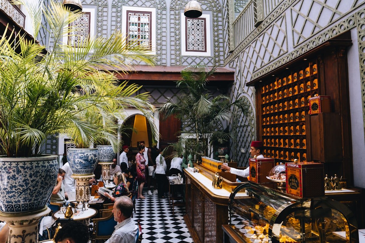 Busy Moroccan-style courtyard cafe with ornate tiled walls and tropical plants