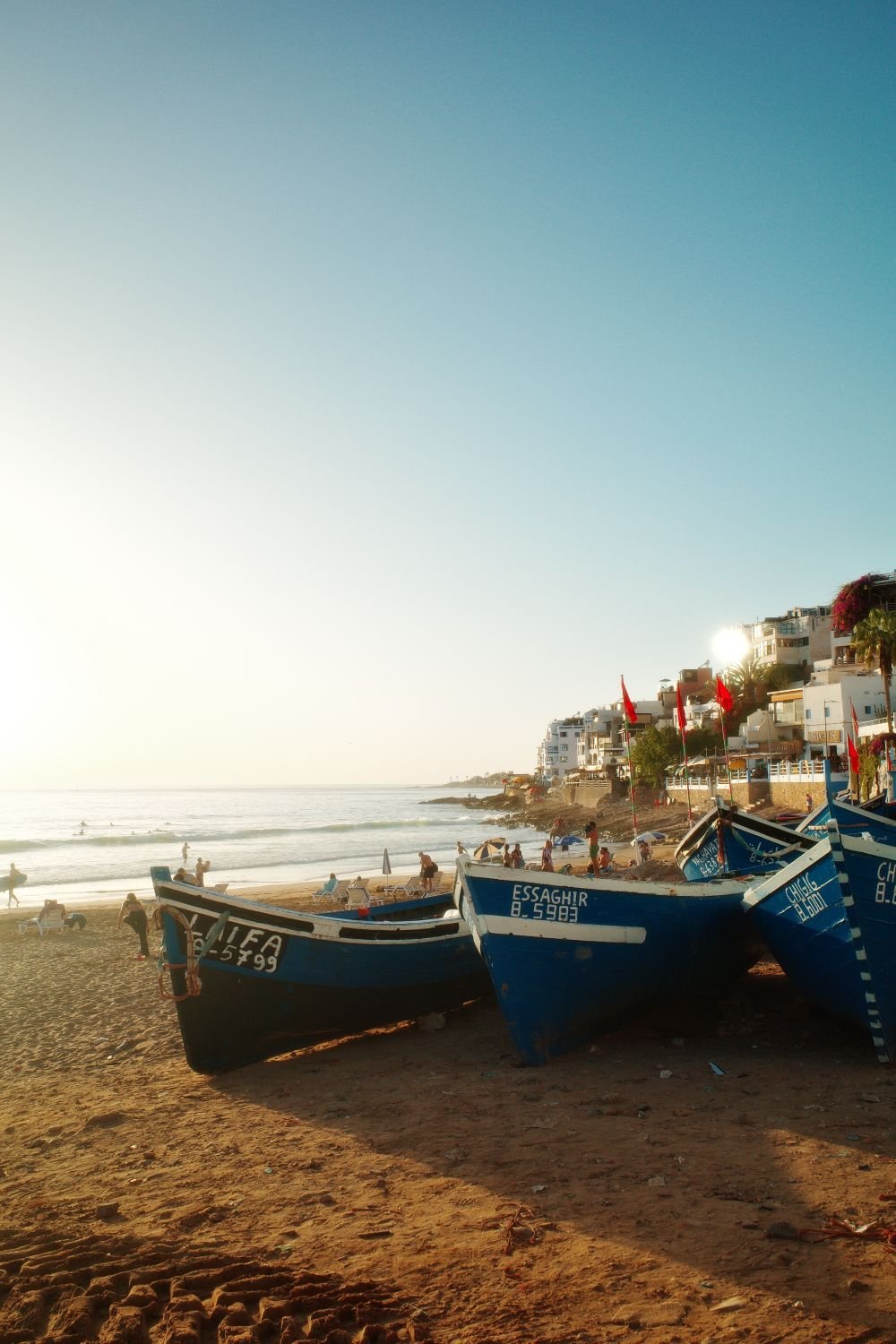 Blue boats on the sand in low sun with the hillside village beyond