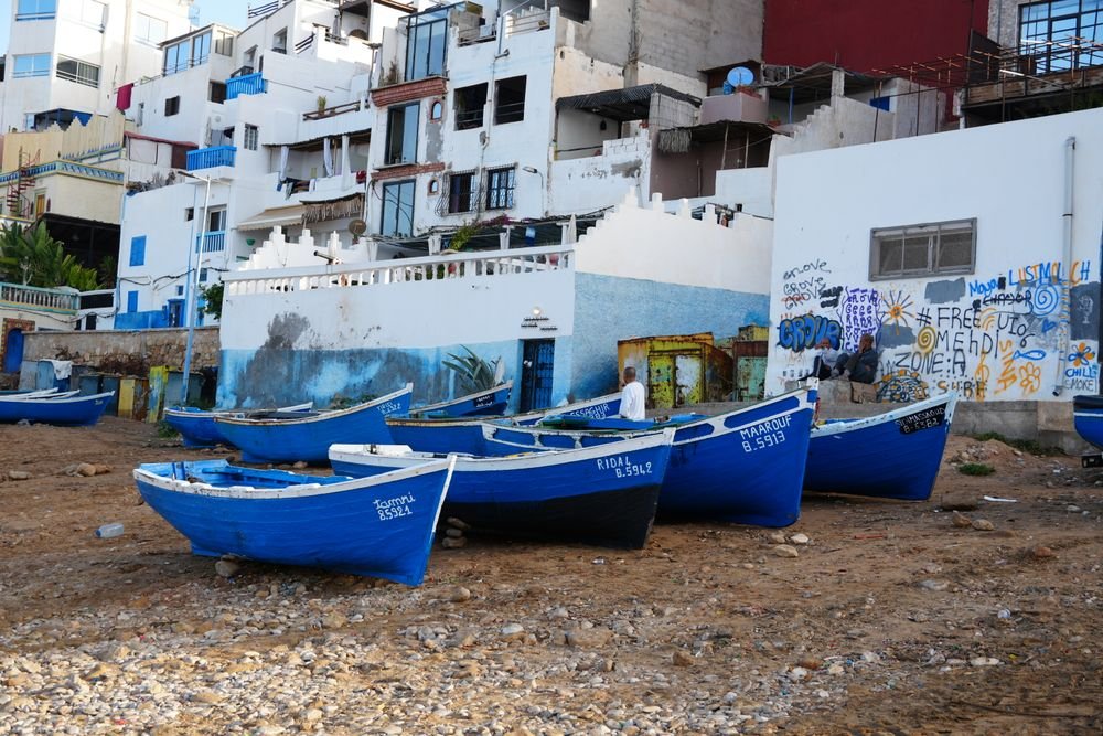 Barcas azules sobre los guijarros junto a casas encaladas con arte urbano