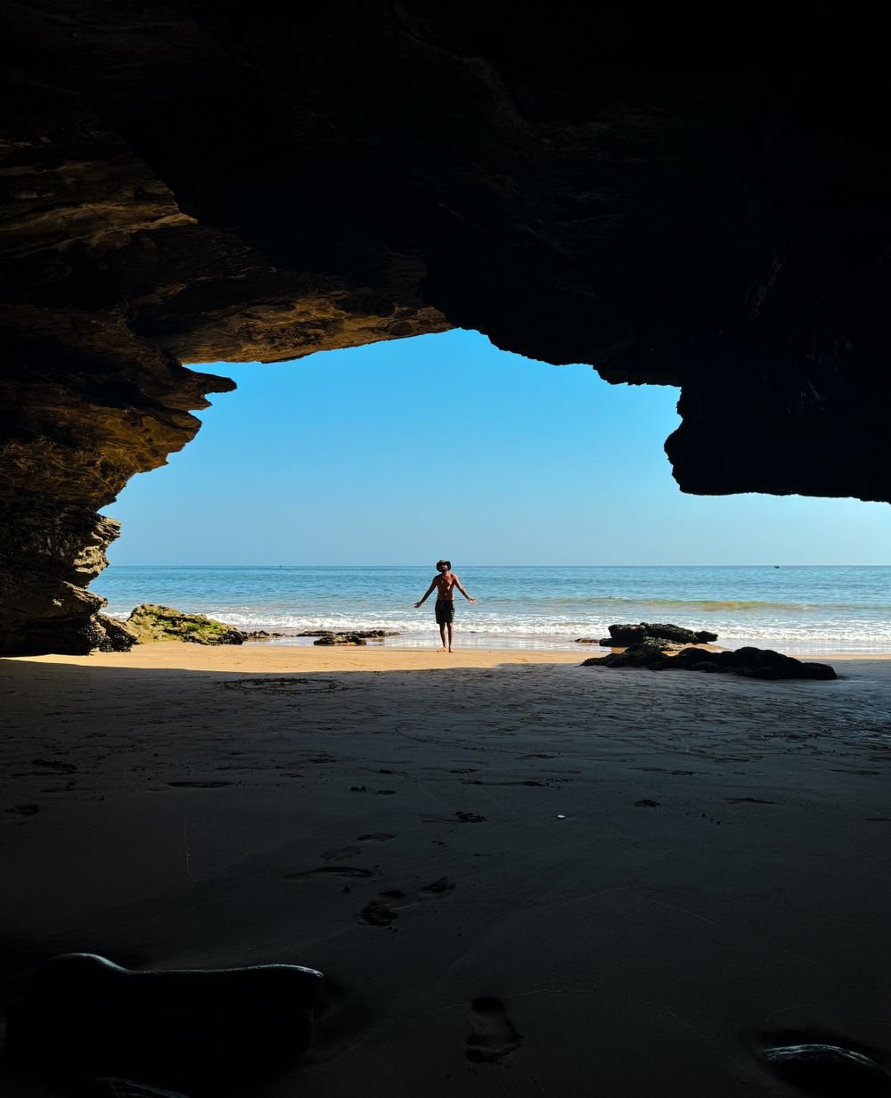 A walker silhouetted in a cave opening looking out to the beach