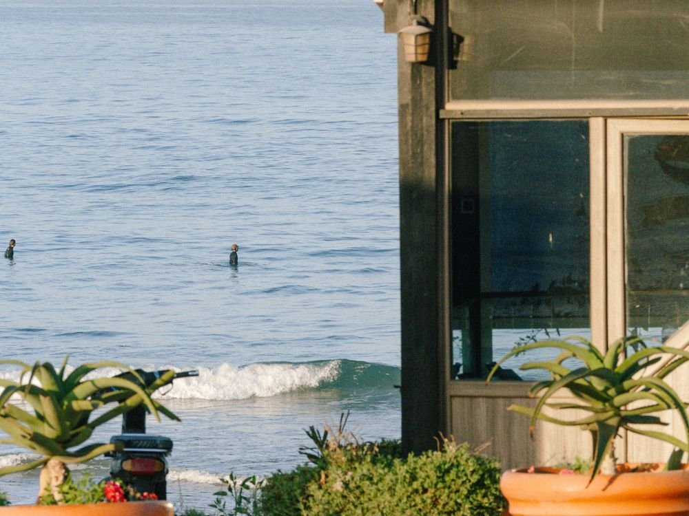 Vista al océano desde una terraza, con surfistas a lo lejos