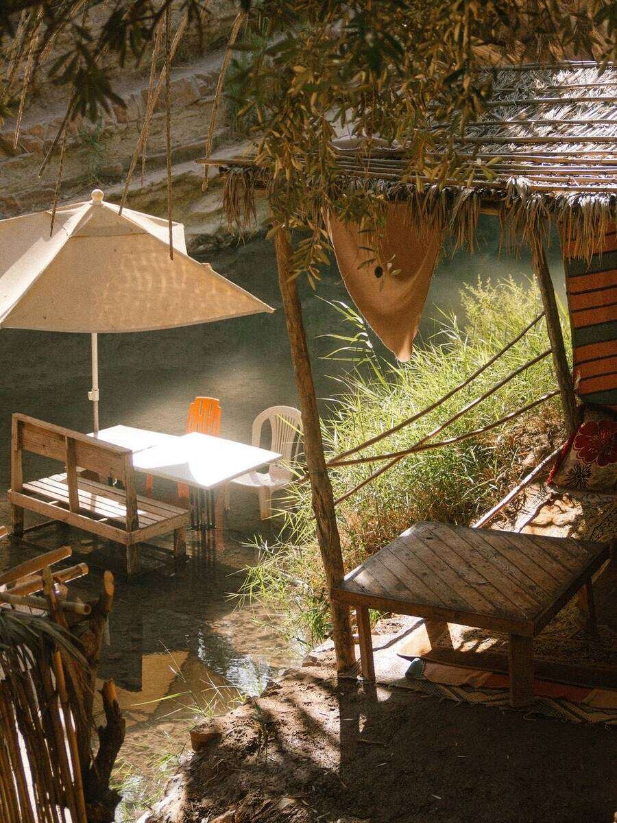 A shaded seating area with a parasol and wooden benches by the river