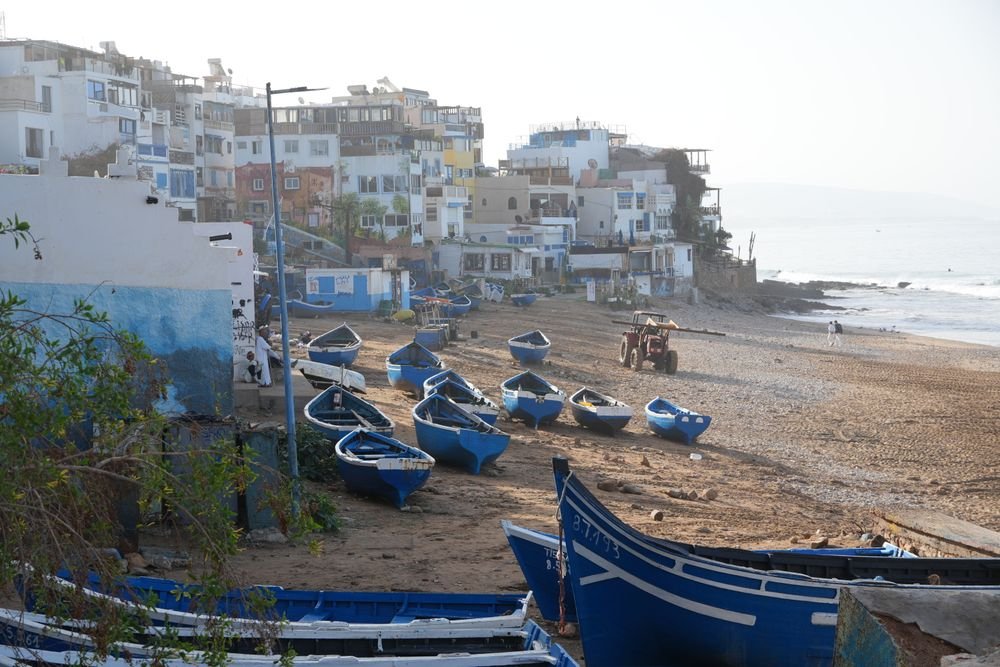 Blue fishing boats on the beach below the white houses of Taghazout
