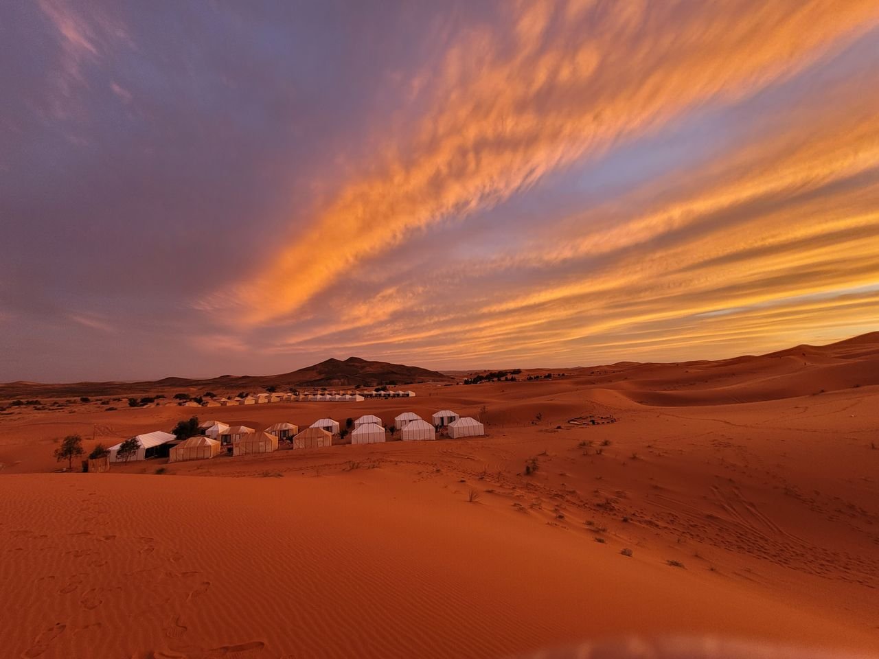 Camp de tentes blanches sous un ciel orange dans le désert