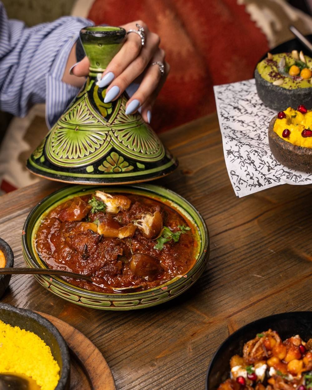 Tajine servido con cuscús y pequeños platos sobre una mesa de madera