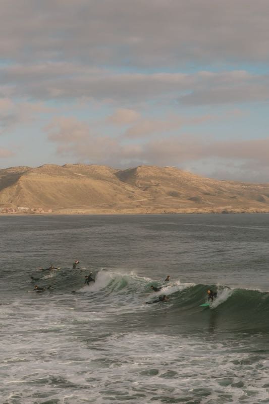 Surfers riding a long wave in Imsouane bay with dry hills behind