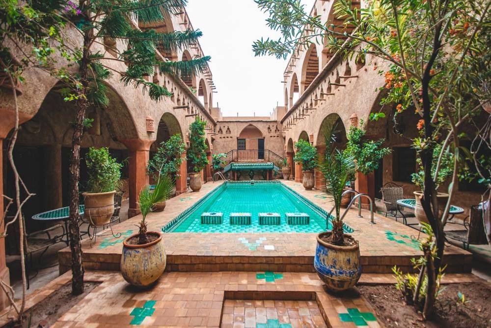 Piscine de cour entourée d'arcades et de plantes dans un riad marocain