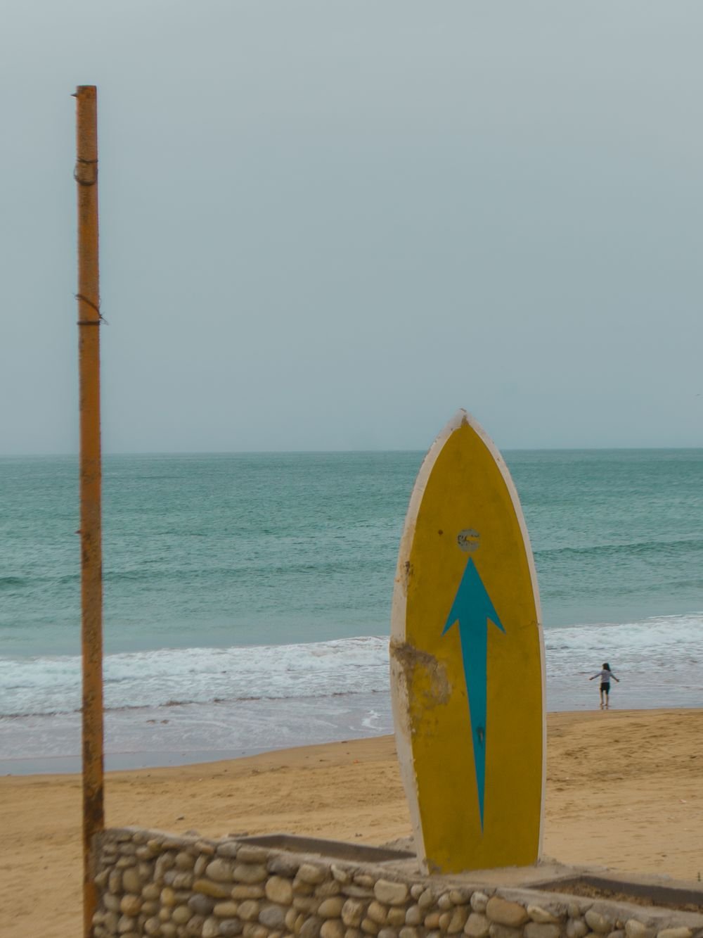 Un panneau en forme de planche de surf sur la plage, indiquant les vagues