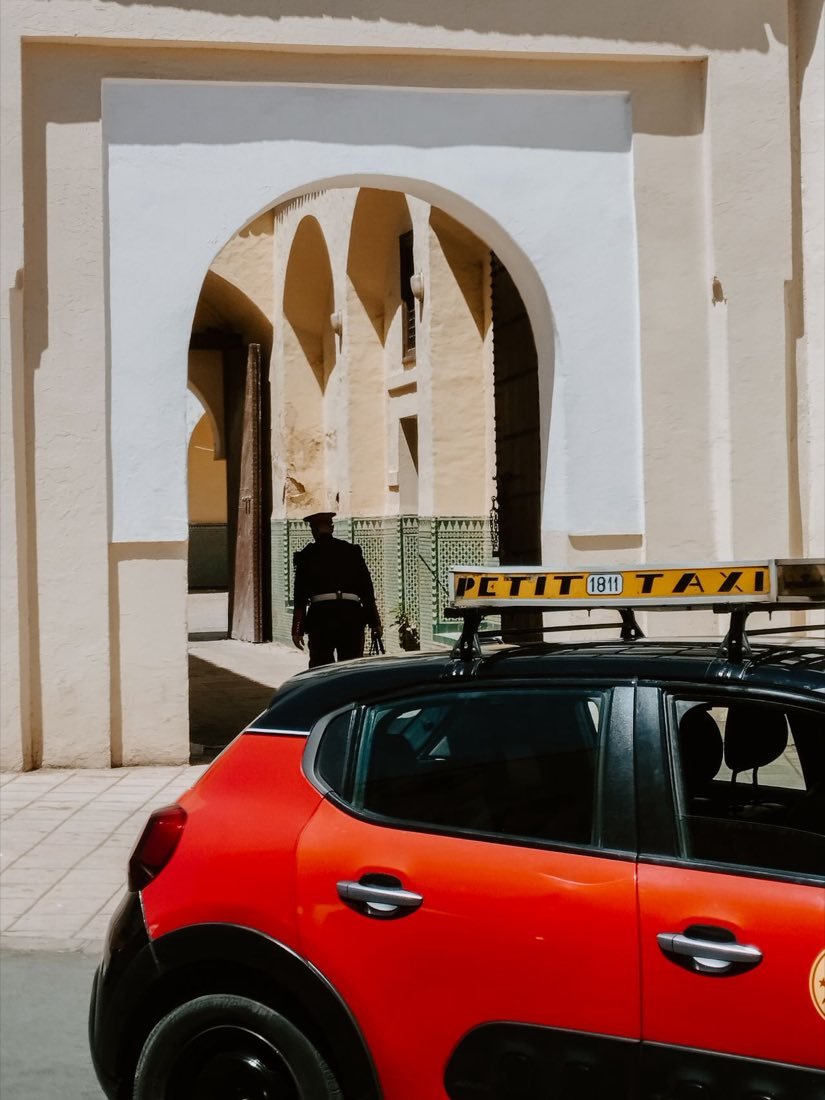 Un taxi rojo frente a una puerta con arco marroquí