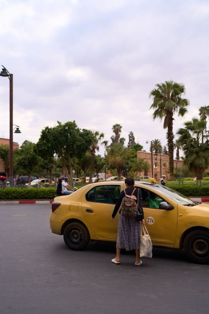 A yellow petit taxi beside a palm-lined avenue