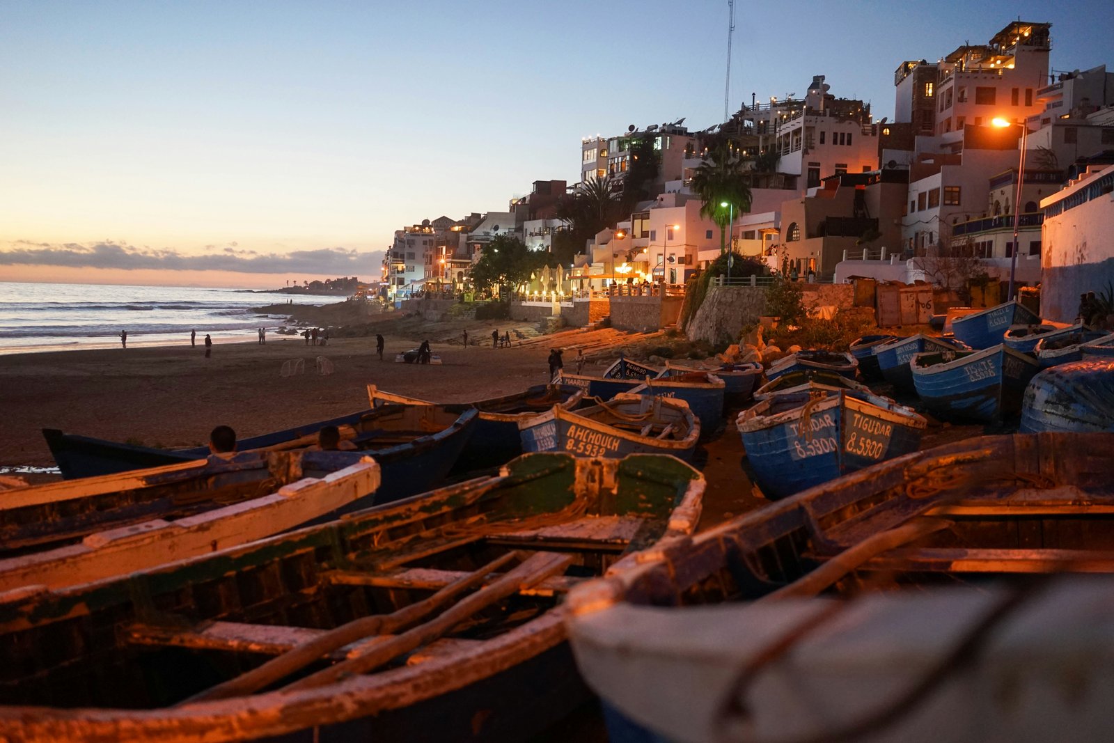 Taghazout village at dusk with fishing boats on the beach and white buildings rising up the hillside