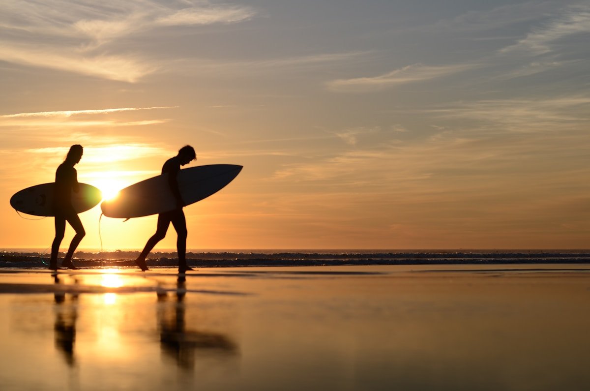 Two surfers carrying boards at sunset on the Moroccan Atlantic coast