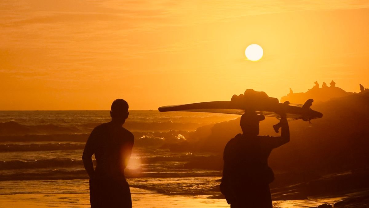 Silhouetted surfers with boards at sunset on Taghazout beach, Morocco