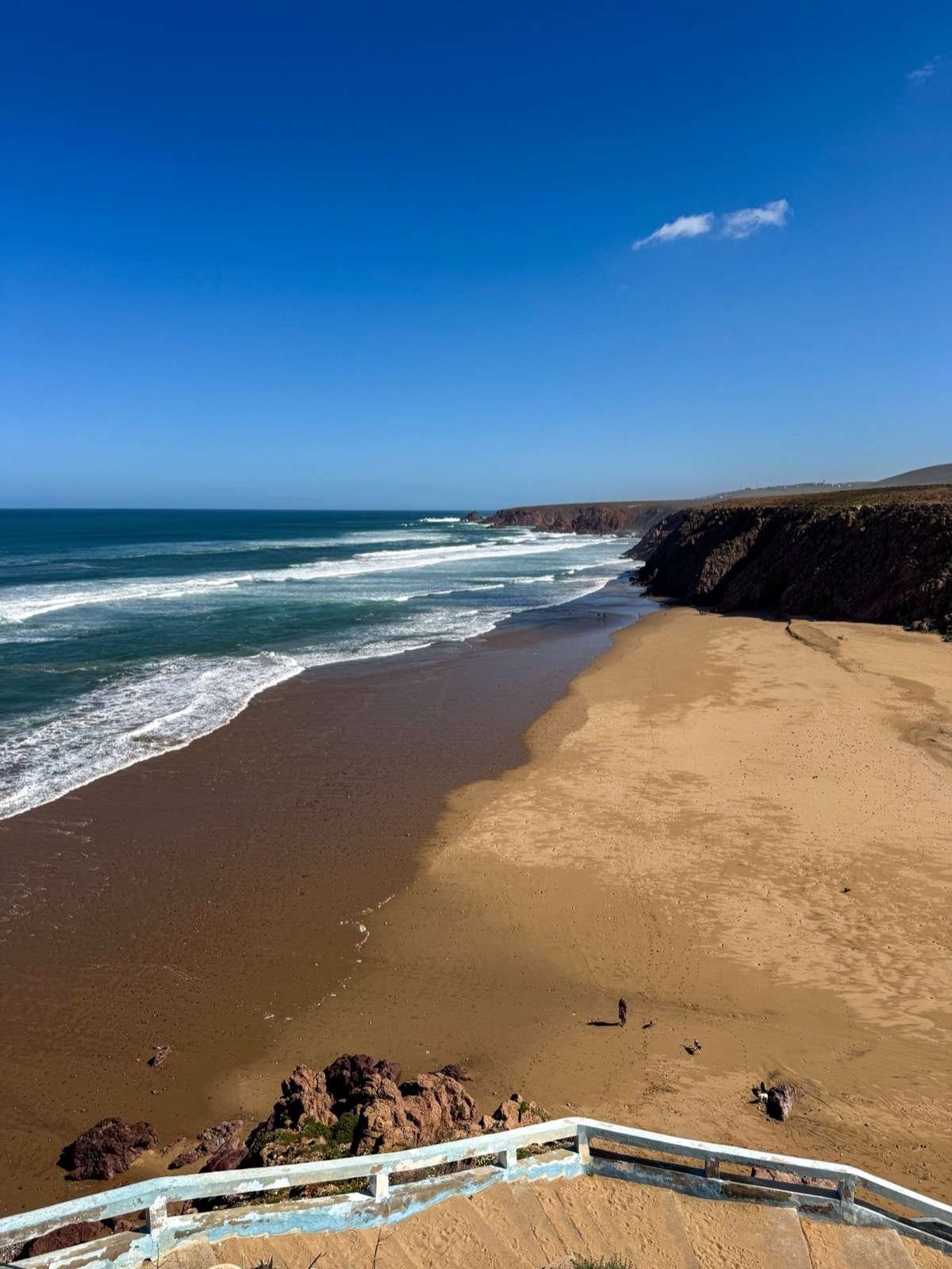 Clifftop view over Mirleft's wide empty beach with reddish rocks and Atlantic waves, southern Morocco