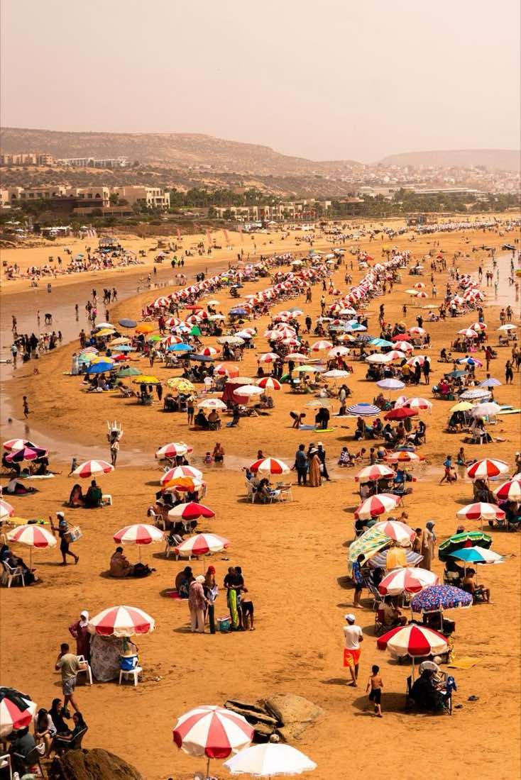 Crowded beach with red and white umbrellas on the Atlantic coast near Agadir, Morocco